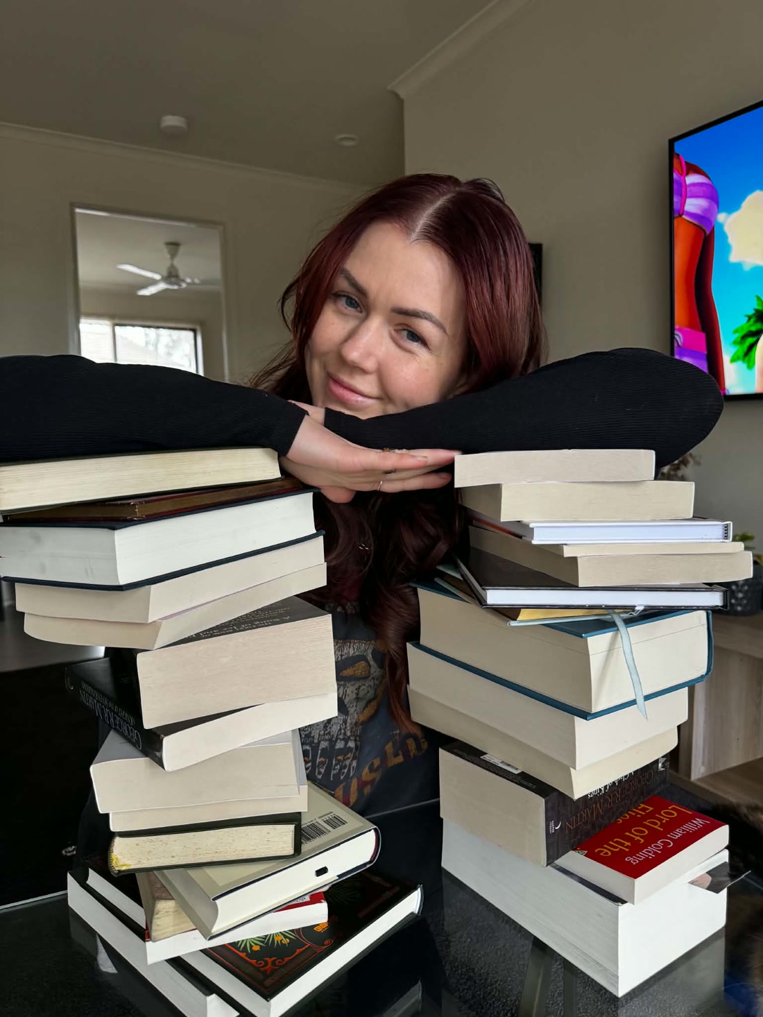 Danii Lee resting her arms on two tall stacks of books.